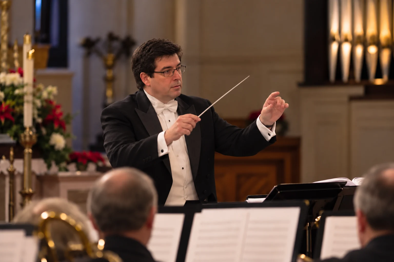 James F. Compton conducting with a baton in a warm church sanctuary, wearing formal black tuxedo and tails.